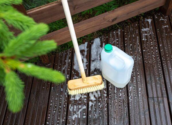 How to Clean and Maintain Decking A broom and soapy water cleaning decking